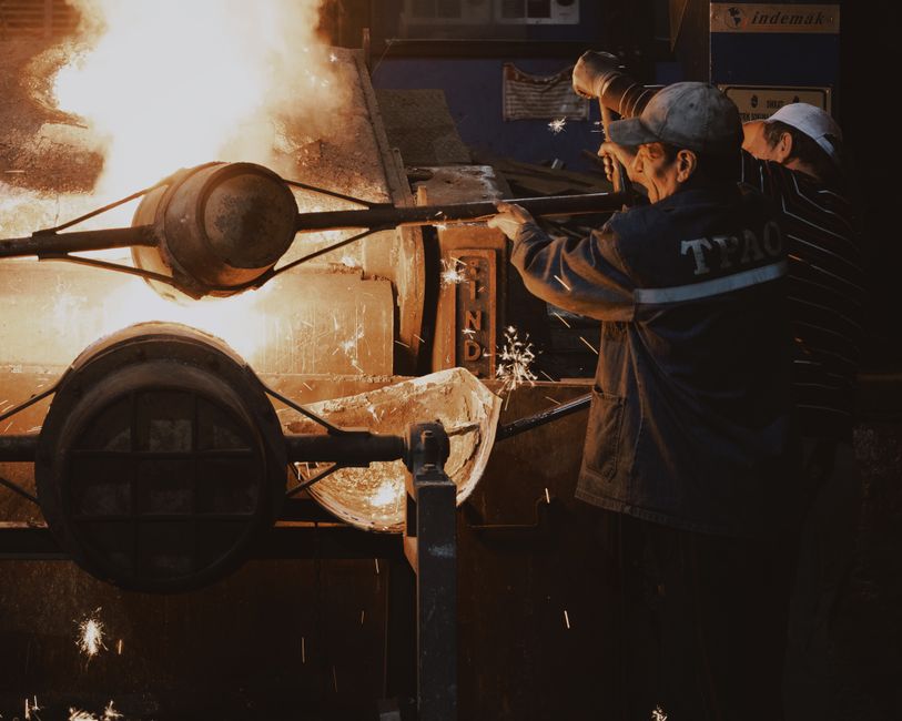Two workers at a foundry pouring molten metal into a mold with sparks flying. (Photo: Mehmet Turgut Kirkgoz / Pexels)