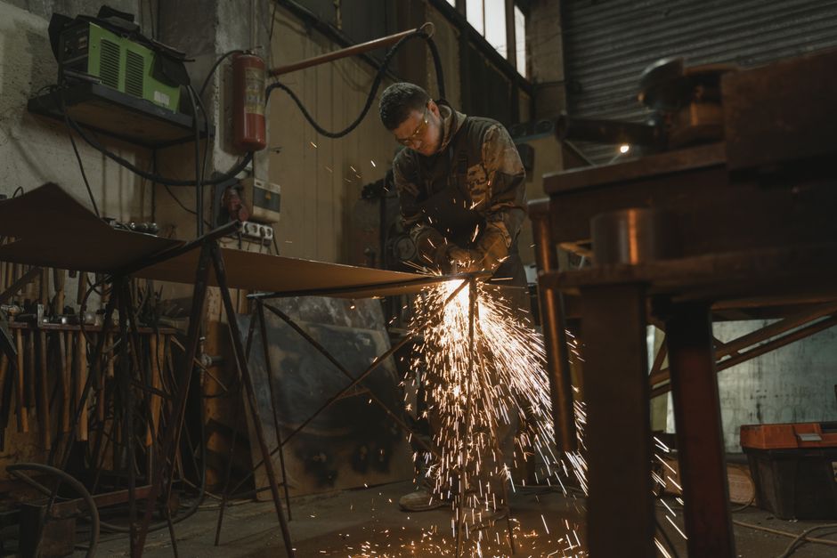 Male welder in safety gear welding metal with sparks in an industrial setting. (Photo: Tima Miroshnichenko / Pexels)