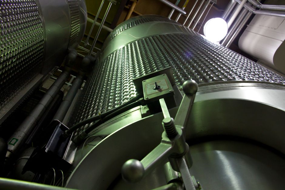 Low-angle shot of large stainless steel tanks inside a modern industrial facility. (Photo: Mark Stebnicki / Pexels)