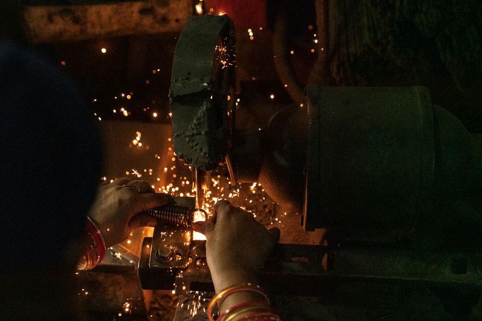 Detailed view of hands working on a metal cutting machine with sparks flying in a dark workshop setting. (Photo: Nishant Aneja / Pexels)