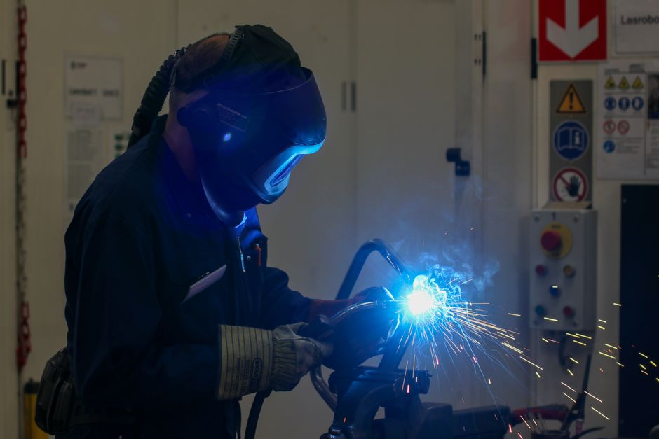 Intense image of a welder working with bright blue sparks flying in an industrial setting. (Photo: Freek Wolsink / Pexels)