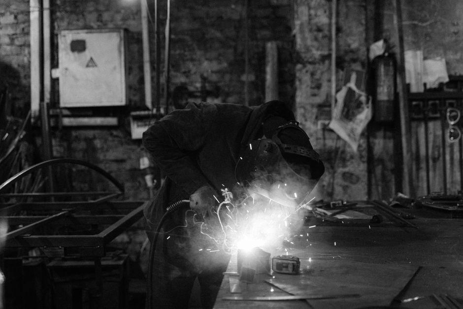 A monochrome image of a welder performing metalwork with sparks flying in an industrial workshop. (Photo: Tima Miroshnichenko / Pexels)
