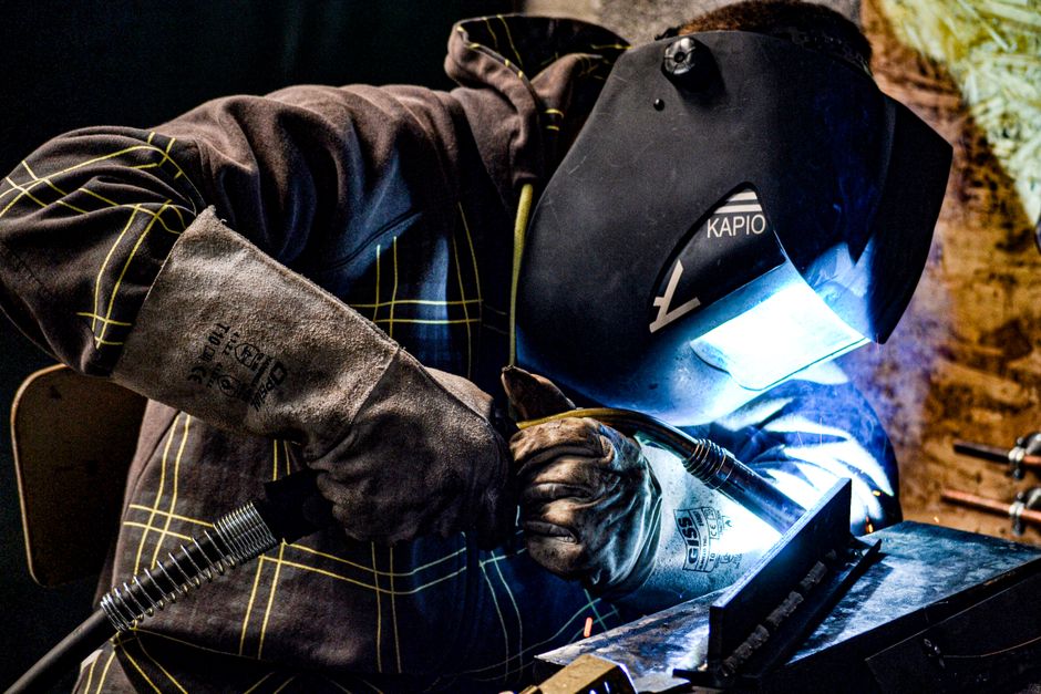 A male welder operates in a factory setting, using protective gear for safety. (Photo: JL Photographie / Pexels)