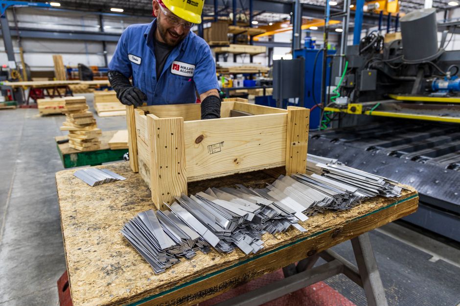 Man in safety gear sorting metal pieces at a factory with wooden crates. (Photo: Rolled Alloys Specialty Metal Supplier / Pexels)